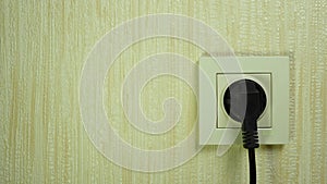 A man`s hand inserts a black electric plug into a white plastic socket on the wall.