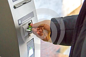 A man`s hand inserts a plastic card into the card receptacle of cash machine