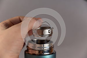 A man`s hand inserts the teapot into the neck of the thermos. Silver brewpot and shiny threaded neck of modern thermos. Turquoise