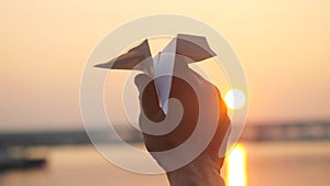 Man`s hand of launch paper plane against the sea during sunset with sun flare and reflections in the water in slowmotion