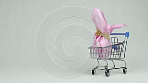Man`s hand lays a pink gift Easter egg in a shopping basket white background, copy space, concept supermarket