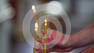 A man's hand lights a candle and places it on a candlestick in a church.