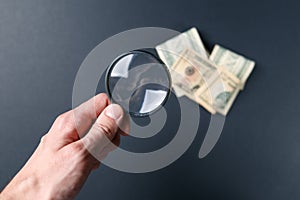 Man`s hand with magnifying glass and money on black background. Paper currency. Looking For Money. Concept of search