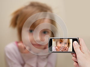 Man's hand making photo of a little girl with a mobile phone.