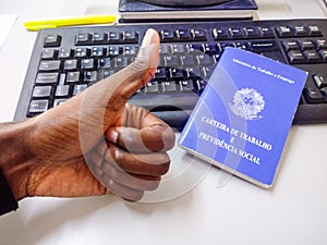 Man`s hand making positive sign thumb up with Brazilian document work and social security and keyboard in the background