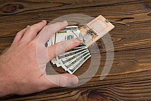 A man`s hand and a mousetrap with bait money dollars banknotes.