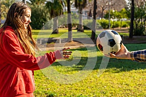 Man& x27;s hand offering a soccer ball to a pretty smiling pre-teen girl to play soccer in the park. The girl wants to