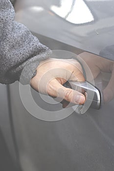 The man& x27;s hand opens the door of the silver-colored car