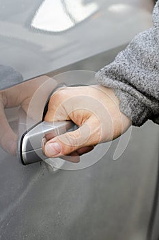 The man& x27;s hand opens the door of the silver-colored car