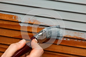 Man`s hand painting wooden panel door with a brush in lead grey colour