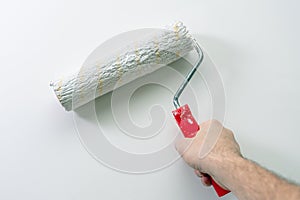 A man's hand paints a wall white with a paint roller