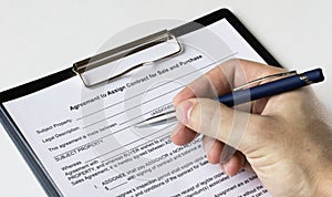 A man's hand with a pen signs a contract in a folder