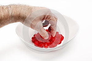 Man's hand picks a cherry from a white bowl with delicious red dried cherries. White background