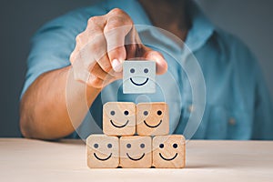 A man\'s hand placing a wooden cube block form with a smiling symbol. The notion of a satisfaction survey is based on the top