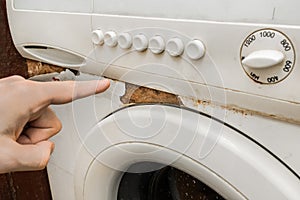A man`s hand points a finger at a trace of rust next to the front keypad of an old broken washing machine. Home appliances wear