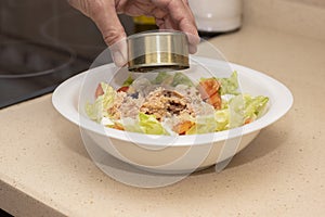 A man`s hand pouring a can of tuna on top of a mixed salad.