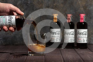 ManÃ¢â¬â¢s hand pouring Herbal Coca-Cola from bottle to ice-filled double old fashioned glass