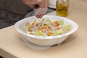 A man`s hand pouring salt into a mixed salad