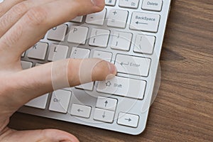 Man`s hand pressing enter button on wireless keyboard on wooden table