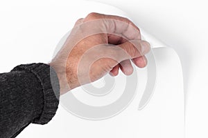 Man`s hand pull up  a bottom corner of a white paper sheet to uncover a neutral foreground with clipping path and copy space for