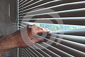 man& x27;s hand pushes back the window blinds on the window