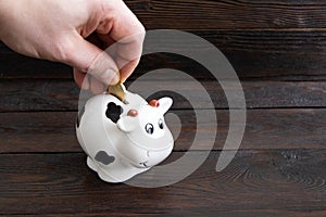 A man`s hand puts a coin in the piggy bank on a wooden background.Saving money. Family budget. Money box on a wooden table.Coin photo