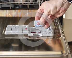 a man& x27;s hand puts a tablet of detergent in the tray for washing dishes in the dishwasher