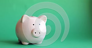 Man`s hand putting coins in piggy bank of pig shape on green background.