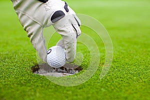 Man's hand putting a golf ball into hole on the