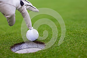 Man's hand putting a golf ball into hole on the