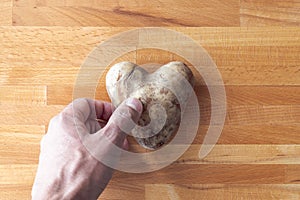 A man`s hand reaches down to pick up a heart shaped potato laying on a wooden cutting board  making a great background symbolizin