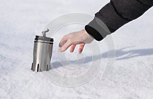 A man`s hand reaches for a thermos with hot coffee in the snow