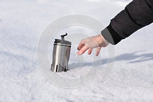 A man`s hand reaches for a thermos with hot coffee in the snow