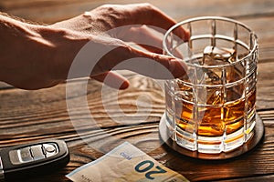 Man`s hand reaching to glass with alcohol drink and car key. Drink and drive concept.