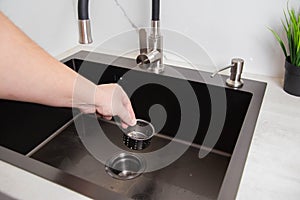 A man& x27;s hand removes a metal strainer from a kitchen sink drain. Cleaning the drain and pipes from clogging with