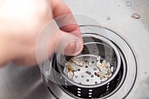 A man& x27;s hand removes a metal strainer from a kitchen sink drain. Cleaning the drain and pipes from clogging with