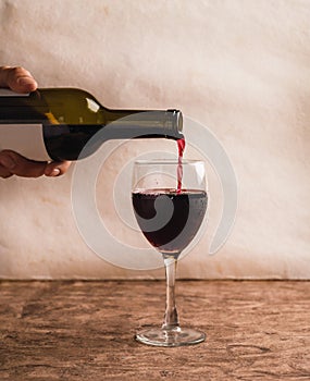 A man`s hand serving a glass of red wine from the bottle, the drops of wine leap from the glass.