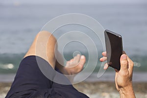 Man& x27;s hand with smartphone against the sea and pebble beach. Close-up