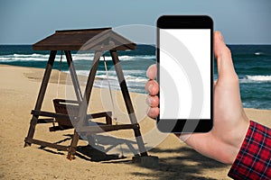 A man`s hand with a smartphone on a beach and ocean background