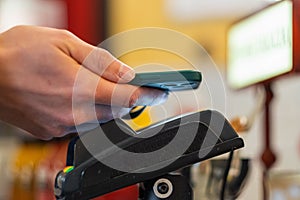 A man& x27;s hand with a smartphone pays with contactless payment through a close-up terminal