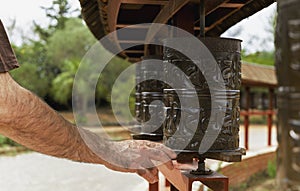 A man's hand spinning a Buddhist prayer wheel, carved with mantras. Buddhist Temple of El Garraf Sakya Tashi Ling, Barcelona