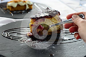 Man`s hand spooning a piece of cheesecake with red fruits jam