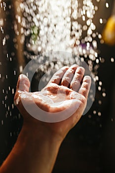 A man`s hand in a spray of water in the sunlight against a dark background. Water as a symbol of purity and life