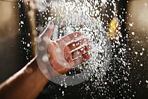 A man`s hand in a spray of water in the sunlight against a dark background. Water as a symbol of purity and life