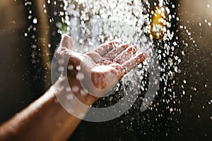 A man`s hand in a spray of water in the sunlight against a dark background. Water as a symbol of purity and life