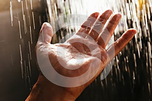 A man`s hand in a spray of water in the sunlight against a dark background. Water as a symbol of purity and life