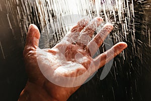 A man`s hand in a spray of water in the sunlight against a dark background. Water as a symbol of purity and life