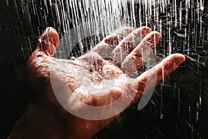 A man`s hand in a spray of water in the sunlight against a dark background. Water as a symbol of purity and life