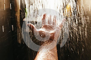 A man`s hand in a spray of water in the sunlight against a dark background. Water as a symbol of purity and life