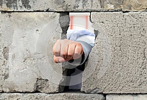 The man`s hand squeezed into a fist smashes through the wall of gray concrete blocks. Symbol of struggle, victory and liberation